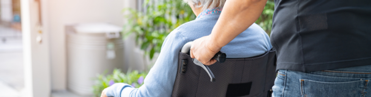 A person is pushing another elderly person in a wheelchair.