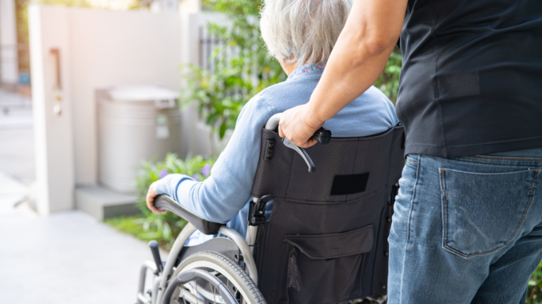 A person is pushing another elderly person in a wheelchair.