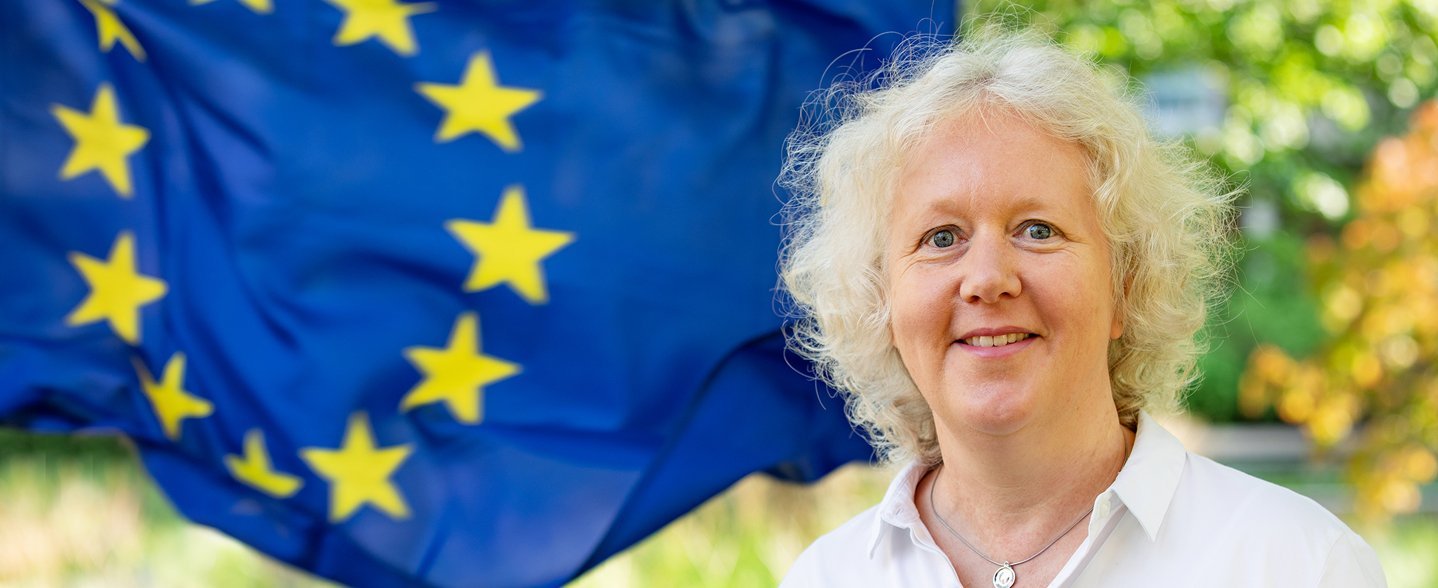 Eine Frau steht vor einer Flagge der Europäischen Union.