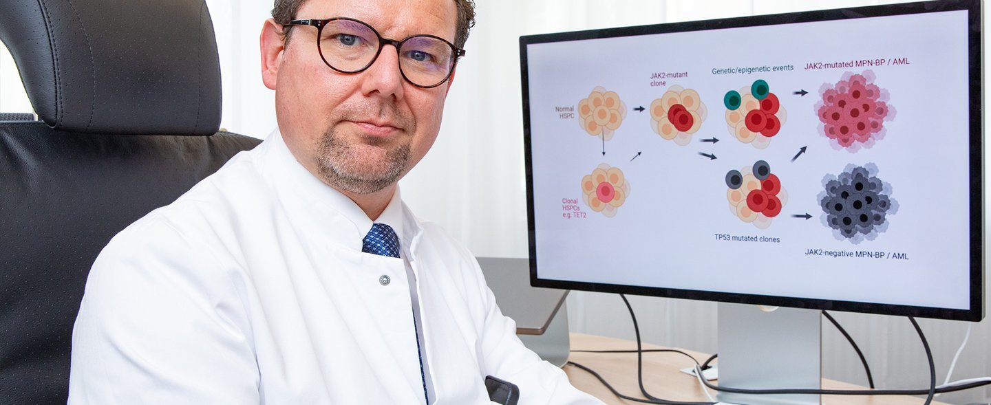 Professor Dr. Florian Heidel sitzt am Schreibtisch und schaut sich am Bildschirm die schematische Darstellung der Entwicklung von Blutkrebs an. 