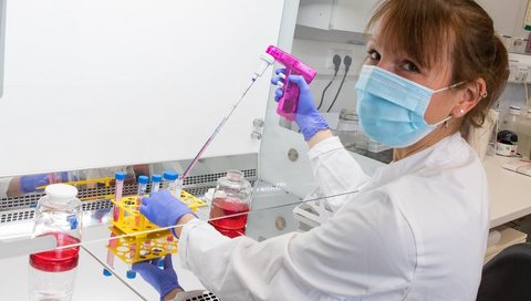 Biologielaborantin Maria Mellin steht an einem Labortisch und füllt Flüssigkeit in Reagenzgläser. 