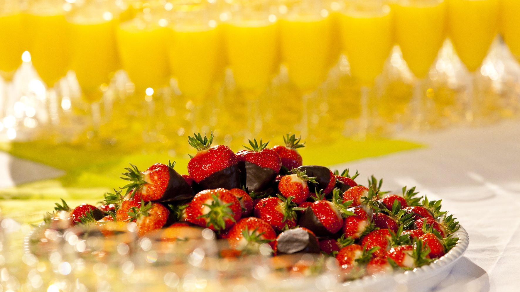 Ein Teller mit Schokoerdbeeren und im Hintergrund sind Gläser mit Orangensaft