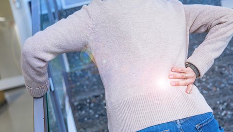 A woman walks up a flight of stairs, bent over, holding her back with her right hand.