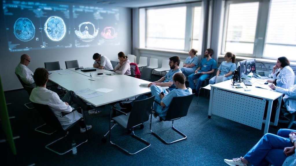 Ein Raumfoto in dem mehrere Ärztinnen und Ärzte sitzen und sich im Rahmen des Molekularen Tumorboards besprechen. An einer Wand sind CT Bilder projiziert.