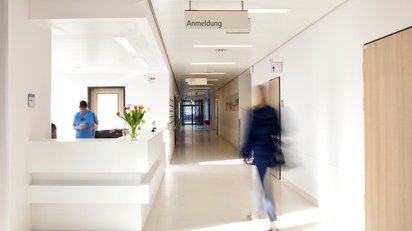 A woman is walking down a corridor. Above her hangs a sign saying "Registration".