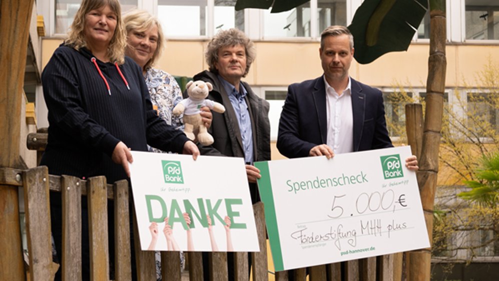 Vier Menschen stehen für die Übergabe des Spendenschecks auf einem Spielschiff im Innenhof der Kinderklinik.