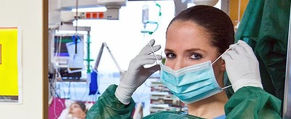 Krankenschwester auf Intensivstation mit Mundschutz, Handschuhen und grünem Kittel