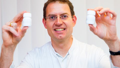 Professor Dr. Michael Heuser hält zwei Medikamentenbehälter in den Händen