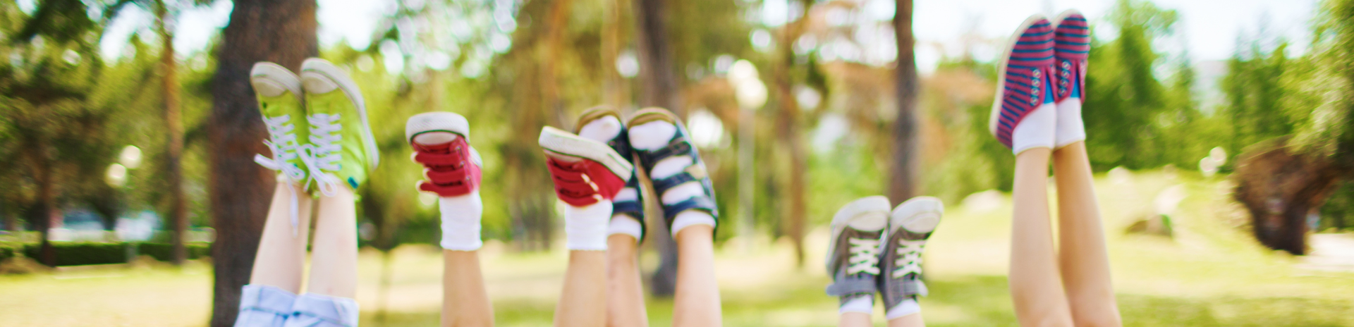 Auf dem Bild sind fünf Kinder zu sehen, welche ihre Füße in Richtung Himmel strecken. Im Hintergrund sieht man einen grünen Park.