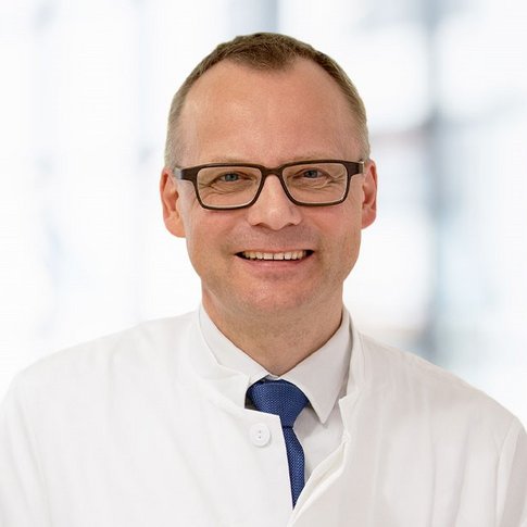 Porträtbild von Heiner Webemeyer, der einen weißen Ärzte-Kittel trägt. 