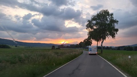 Ein Organspende-Campervan fährt auf einer leeren Landstraße. Am Himmel zeichnet sich ein Regenbogen ab.