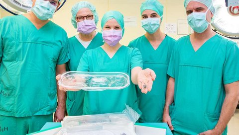 Five doctors in green surgical gowns stand side by side and show the port system.