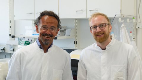 Zwei Forscher in weißen Kitteln stehen in einem Labor.