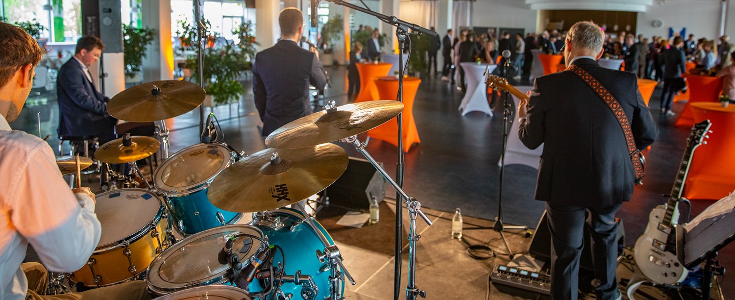 Eine Band spielt in der MHH-Mensa vor vielen Menschen, die teilweise an Stehtischen stehen.