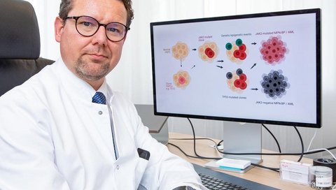 Professor Dr. Florian Heidel sitzt am Schreibtisch und schaut sich am Bildschirm die schematische Darstellung der Entwicklung von Blutkrebs an. 