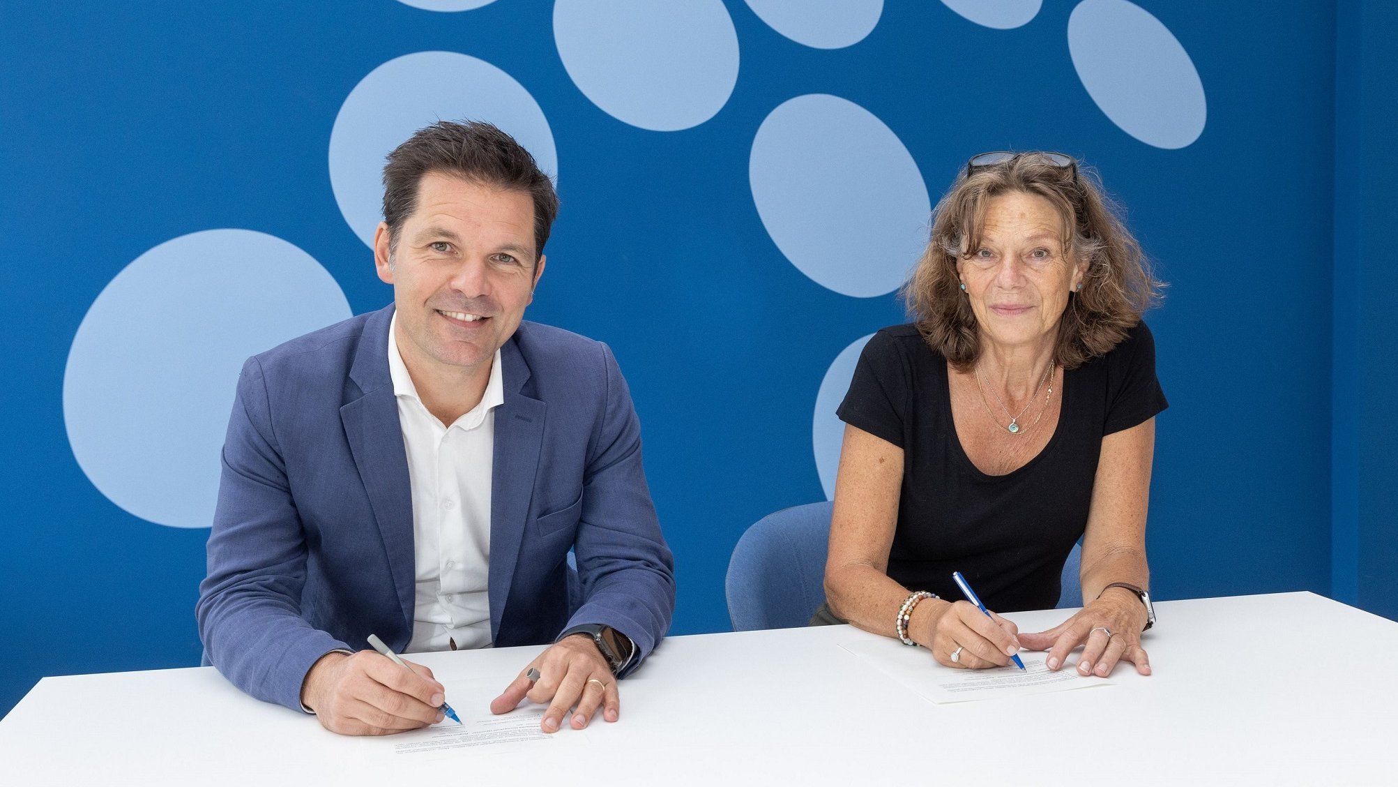 Regional President Steffen Krach and MHH President Denise Hilfiker-Kleiner sit next to each other at a table and sign a document.