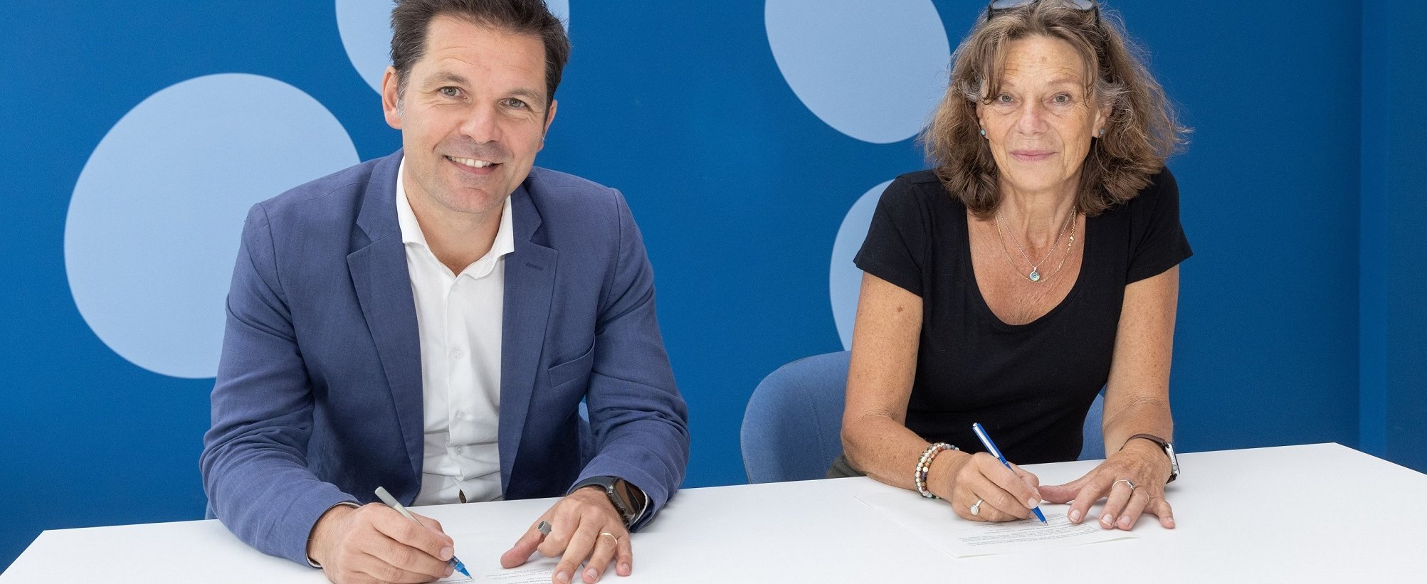 Regionspräsident Steffen Krach und MHH-Präsidentin Denise Hilfiker-Kleiner sitzen nebeneinander an einem Tisch und unterschreiben auf einem Papier.