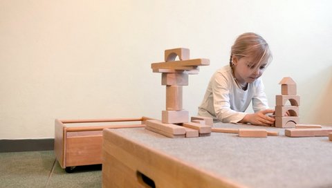 Ein Mädchen spielt mit Holzbauklötzen an einem Tisch. 