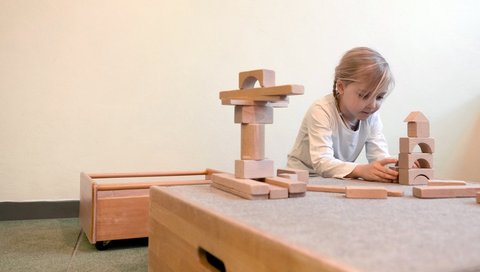  A girl plays with wooden building blocks at a table. 