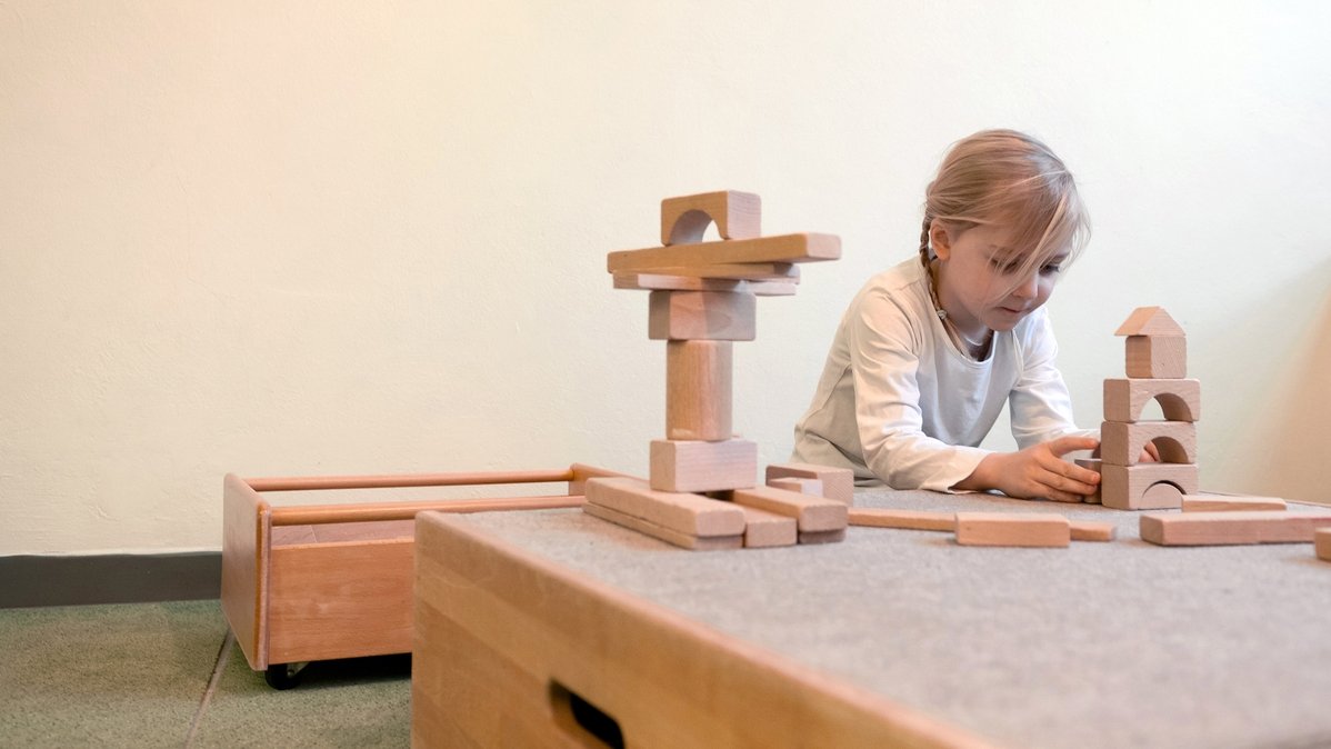 A girl plays with wooden building blocks at a table.
