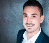 Porträtbild von David Göbel, der eine weißes Hemd mit dunkler Anzugjacke trägt. 