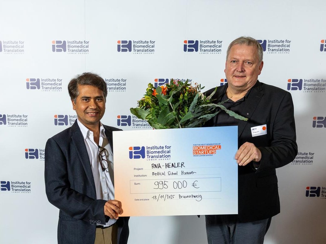 Zwei Männer halten einen Blumenstrauß und symbolischen Förderbescheid in den Händen.