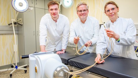 Dr. Blach, Professor Christiansen and Dr. Meinecke (from left) stand in front of the device for interstitial brachytherapy and hold thin tubes in their hands.