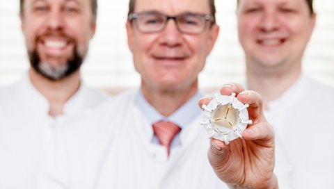 Three doctors in white coats, one holding the new prosthesis for the tricuspid valve.