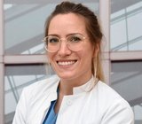 Porträtbild von Kira Glowienka, die einen weißen Arztkittel trägt. 