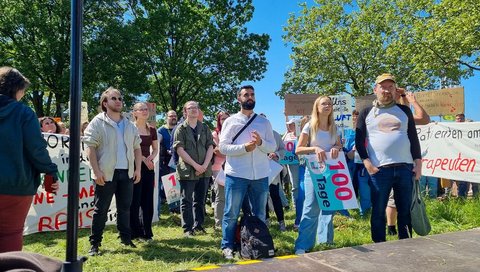 Several people stand at a rally in front of the MHH campus. 