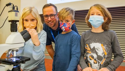 Professor Dr. Nico Lachmann steht zwischen 3 Kindern im Hörsaal.