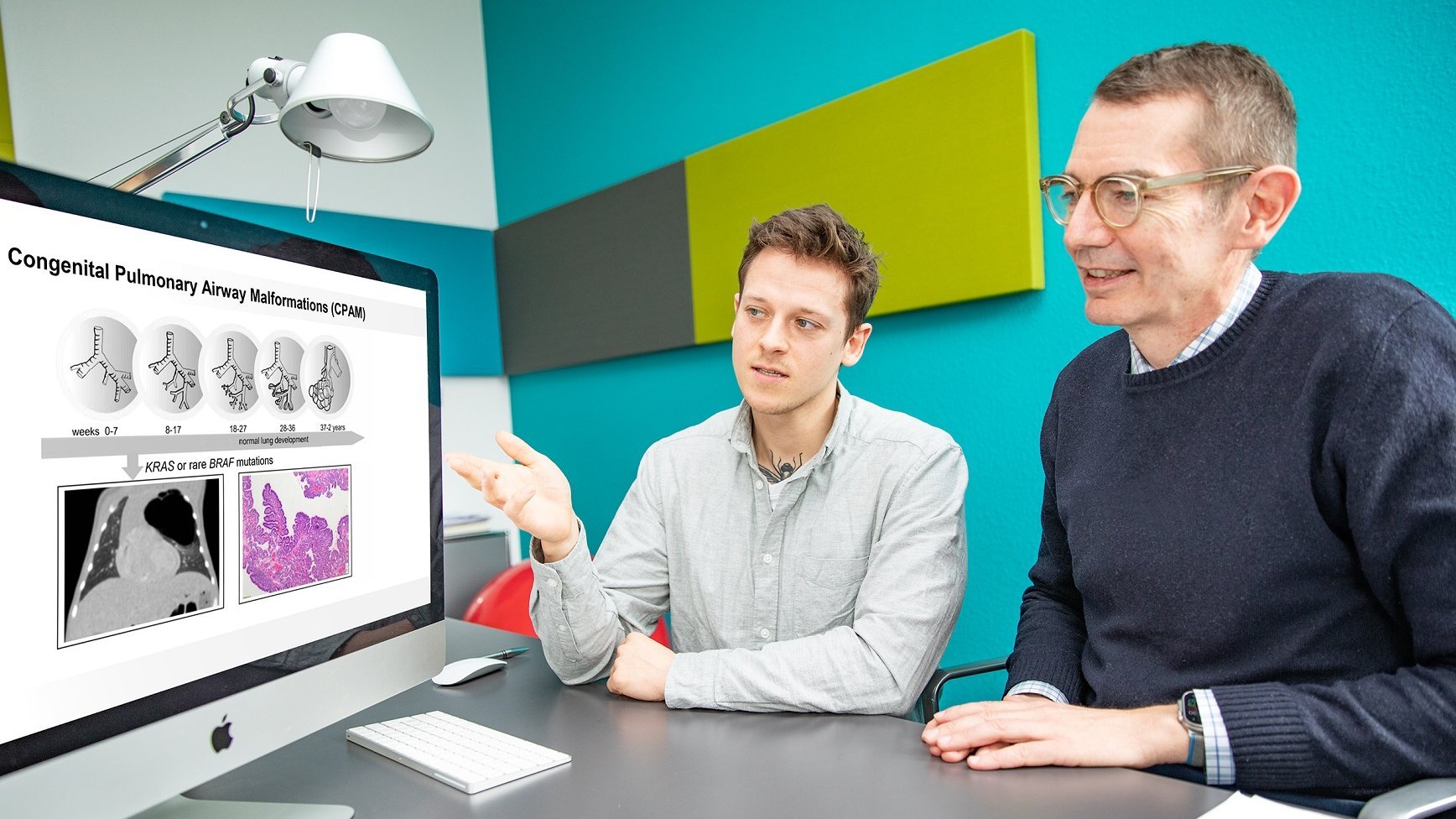 Two men sit at a desk and look at images of the lungs on a screen.