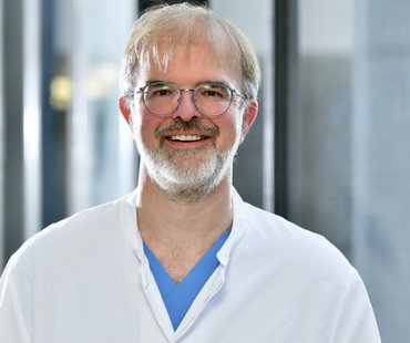 Porträtbild von Holger Leitolf, der einen weißen Arztkittel trägt. 