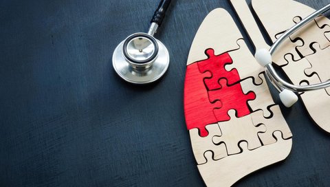 A stethoscope lies next to a lung-shaped puzzle made of light and red puzzle pieces.