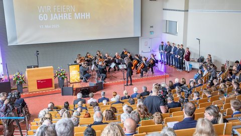 Blick von oben in den Hörsaal F, in dem der Festakt 60 Jahre MHH stattfindet. Viele Meschen sitzen in den Reihen, vorne spielt ein Orchester. 