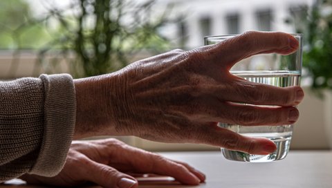 Eine ältere Hand, die ein Wasserglas hält.