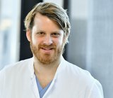Porträtbild von Nils Jedicke, der einen weißen Arztkittel trägt.