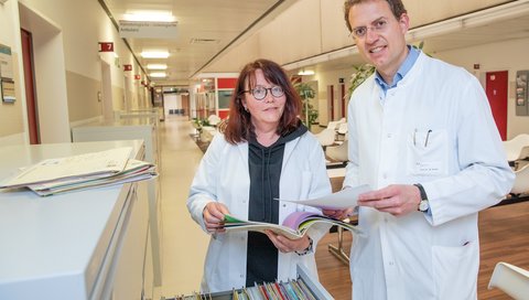 Study Nurse Gabriele Simon and Professor Dr Michael Heuser stand in front of a cabinet with patient files.