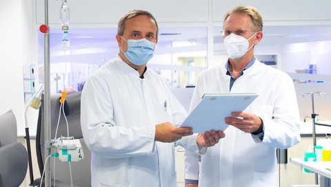   Two doctors stand in a treatment room for amyloidosis patients and discuss.