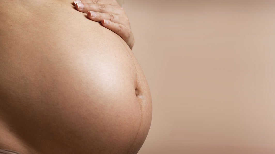 linke Bildhälfte zeigt einen hochschwangeren Bauch mit aufgelegter Hand auf tongleichem Hintergrund