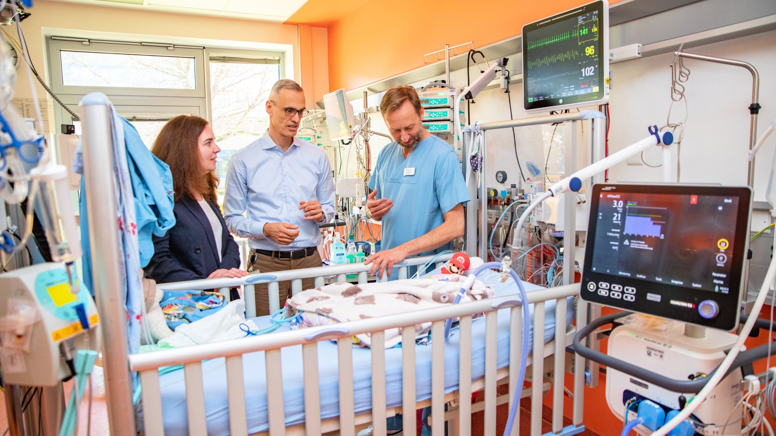 Professorin Dr. Helena U. Zacharias, Dr. Bernd Auber und Privatdozent Dr. Thomas Jack stehen an einem Intensivbett für Neugeborene.