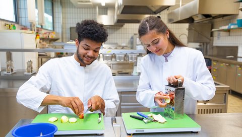 Chigozie Nebo und Kateryna Zinchenko stehen in der Lehrküche der Diätschule und bereiten Essen zu.