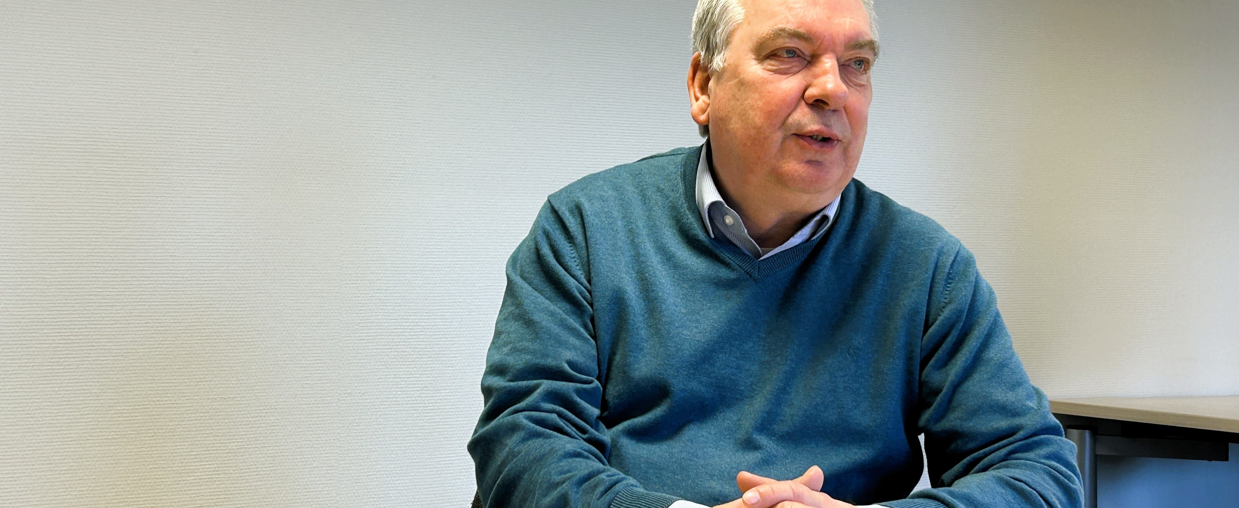 Bernd Günther sitzt an einem Tisch und hält die Hände gefaltet. 