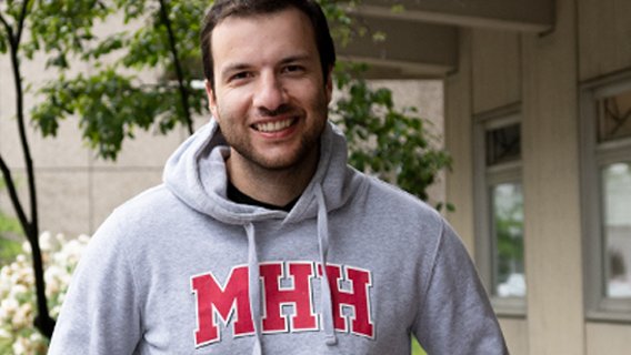 Dr. Alexandros Rahn steht im Unipulli mit MHH-Emblem vor der Kinderklinik.