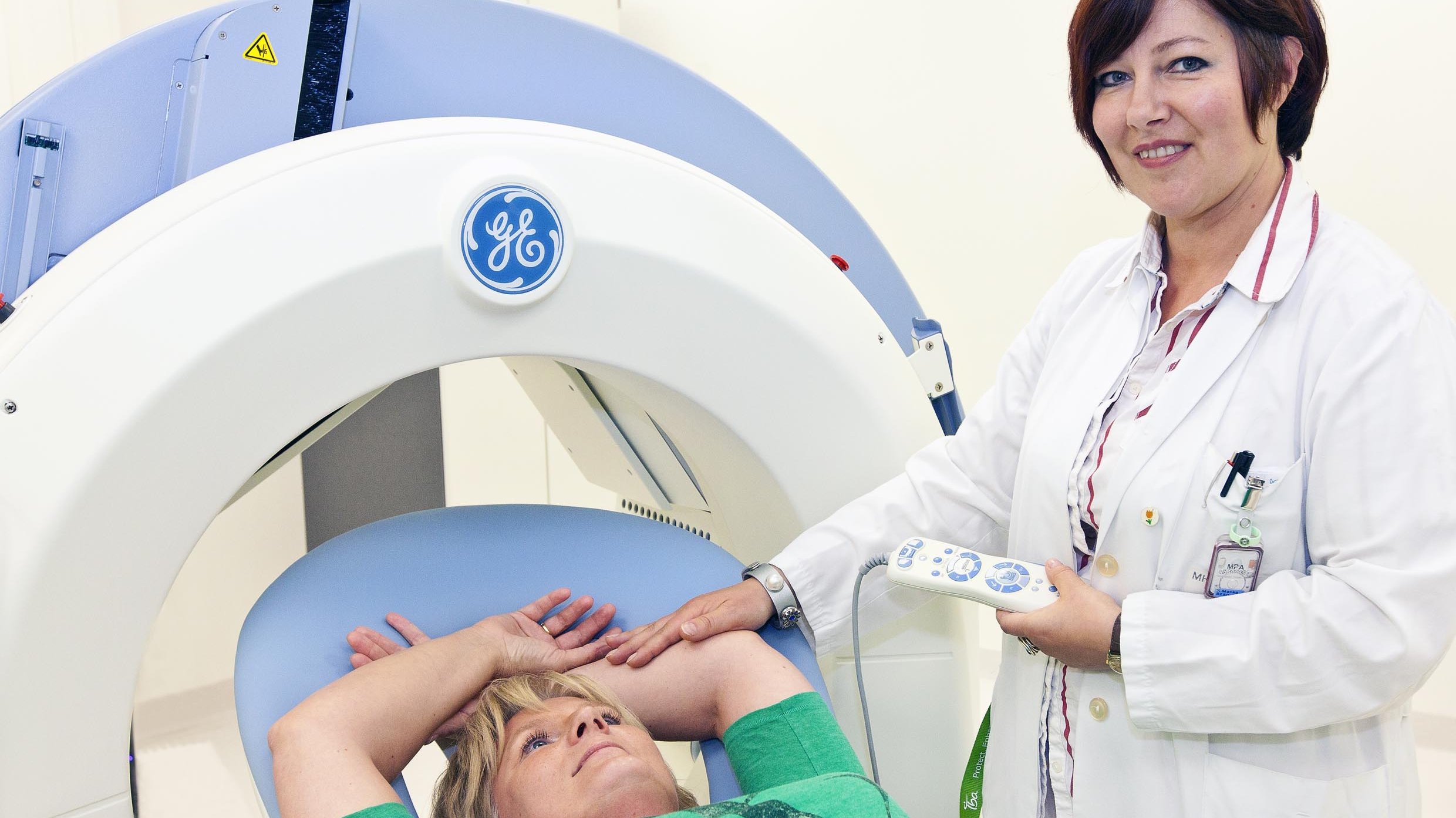 A woman is lying in front of a X-ray machine. A doctor is standing next to her.