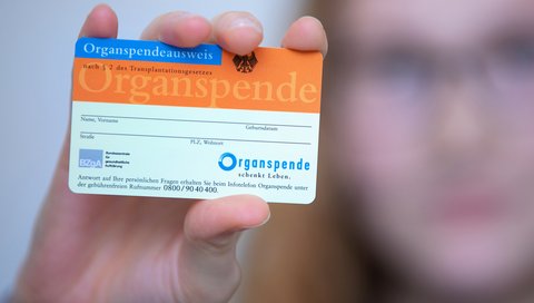 eine Frau hält einen Organspendeausweis in die Kamera. Ihr Gesicht ist unscharf im Hintergrund