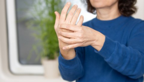 A woman in a blue sweater feels the joints in her fingers.