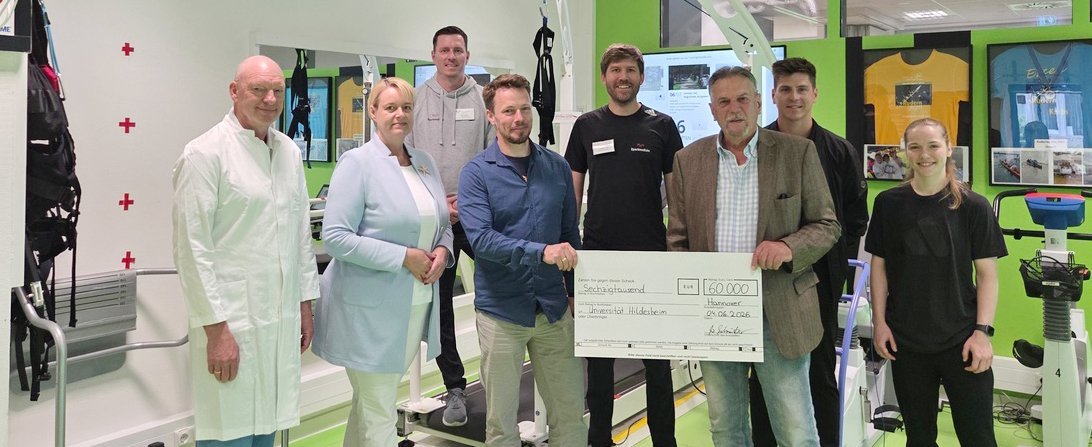 Mehrere Personen stehen als Gruppe zusammen und schauen in die Kamera. Zwei Personen halten einen großen symbolischen Spendenscheck fest.