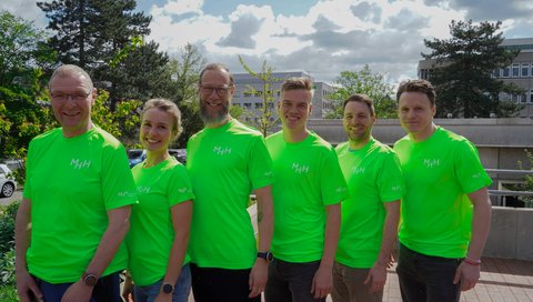 6 Menschen in leuchtend grünen Sport-Shirts mit weißem MHH-Aufdruck auf der Brust und dem Ärmel