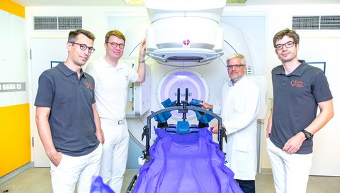 Four doctors from radiotherapy and cardiology stand at a device for high-precision radiation. Alternative caption 